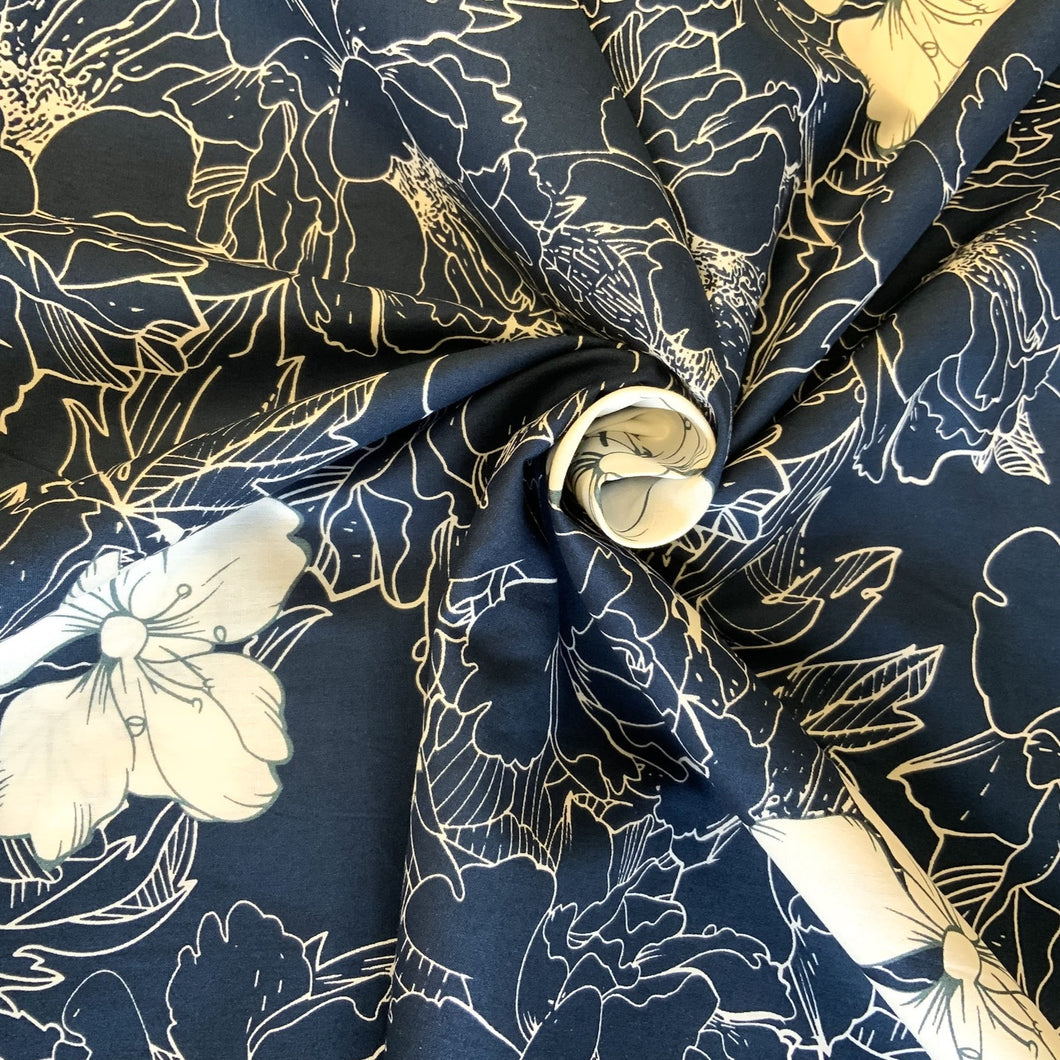 A cotton poplin fabric with a design inspired by the Mallow flower in a white stencilled style along with the flower in contrasting white, against a navy background. The cotton poplin has a smooth handle and a slight drape, it would be a perfect sewing fabric for dressmaking projects or craft.