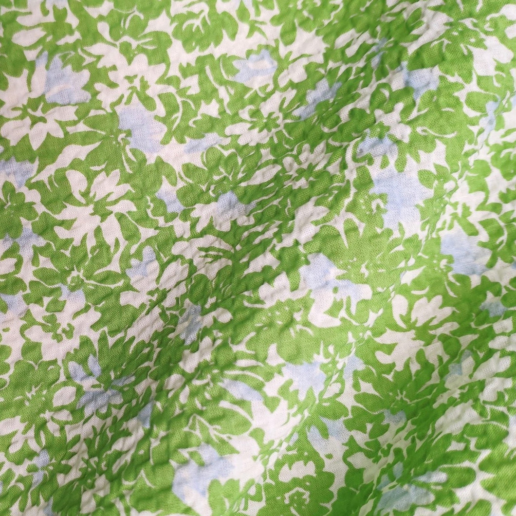 The cotton seersucker fabric is a delightful choice with its unique design and characteristics. It features a pattern of green lush little flowers with blue embellishments, creating a charming and vibrant appearance. The fabric is from Pigeon Wishes available at Lush Cloth